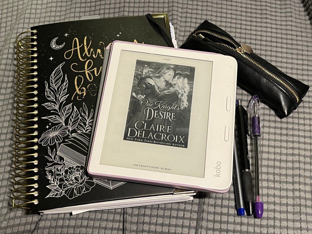 Kobo ereader showing cover of One Knight's Desire by Claire Delacroix with Always Fully Booked planner, pens, and pencil case in the background.